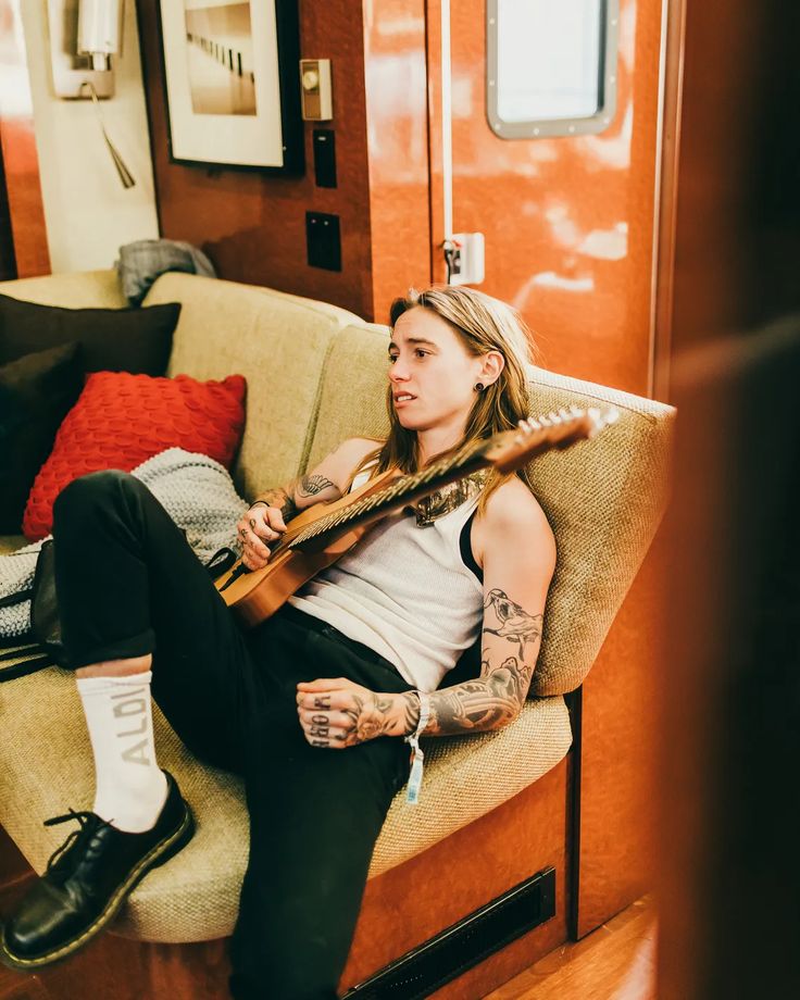 a woman sitting on top of a couch with a guitar in her hand and tattoos on her arm