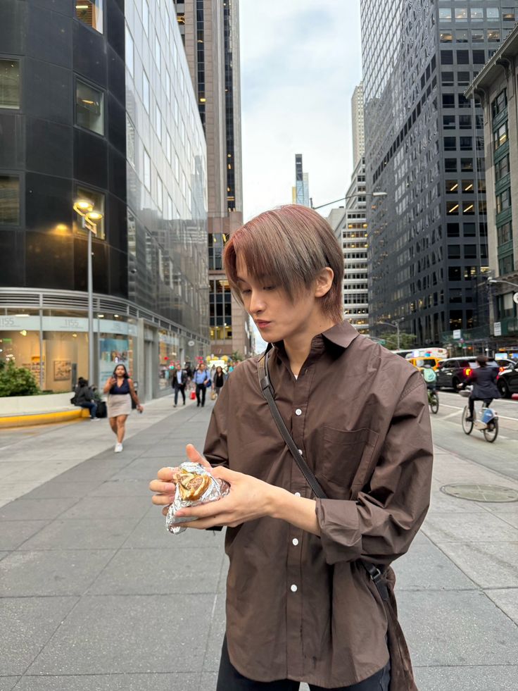 a woman is standing on the sidewalk and looking at her cell phone while holding something in her hand