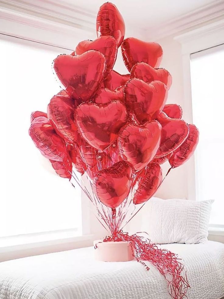 a bunch of red heart shaped balloons sitting on top of a bed next to a window