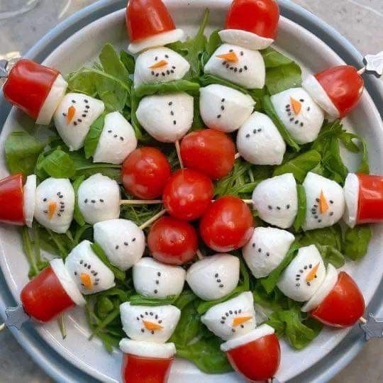 a white plate topped with tomato and mozzarella snowmen on skewers