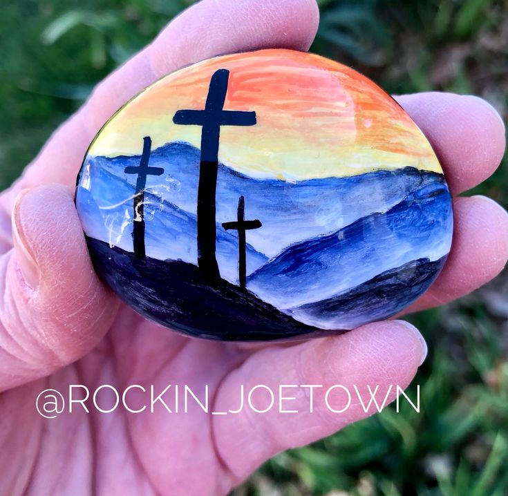 a hand holding a painted rock with a cross on it