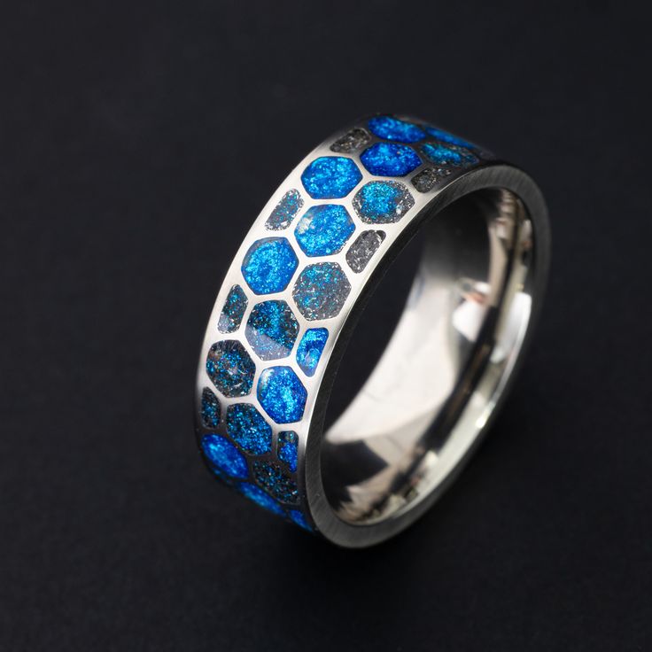 a blue and silver ring with hexagon tiles on it's side, sitting on a black surface