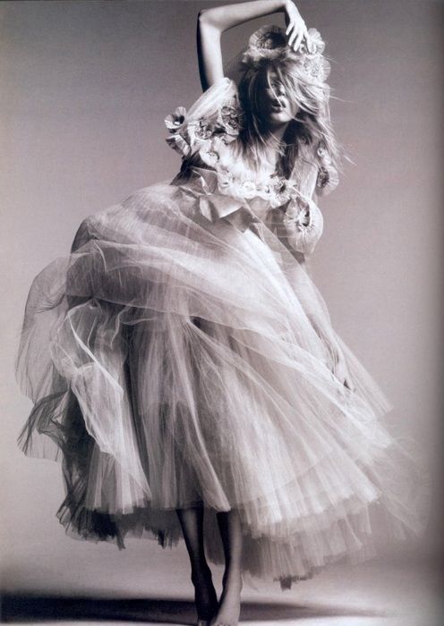 a black and white photo of a woman in a tutu skirt with her arms behind her head