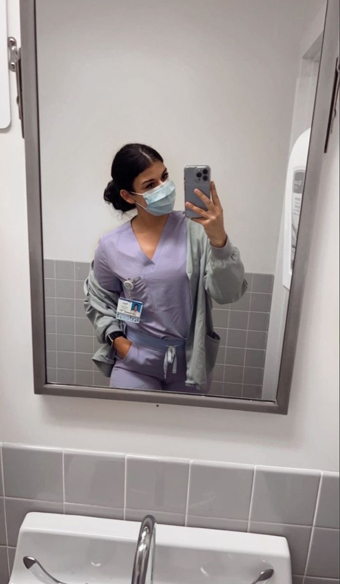 a woman taking a selfie in front of a bathroom mirror wearing a face mask