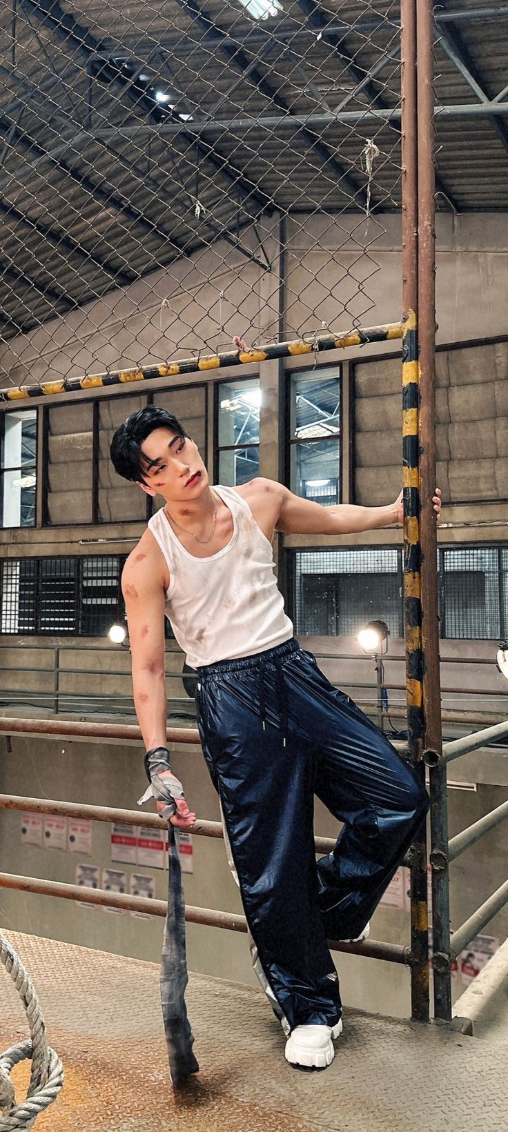 a man leaning on a fence holding a baseball bat in his right hand and posing for the camera