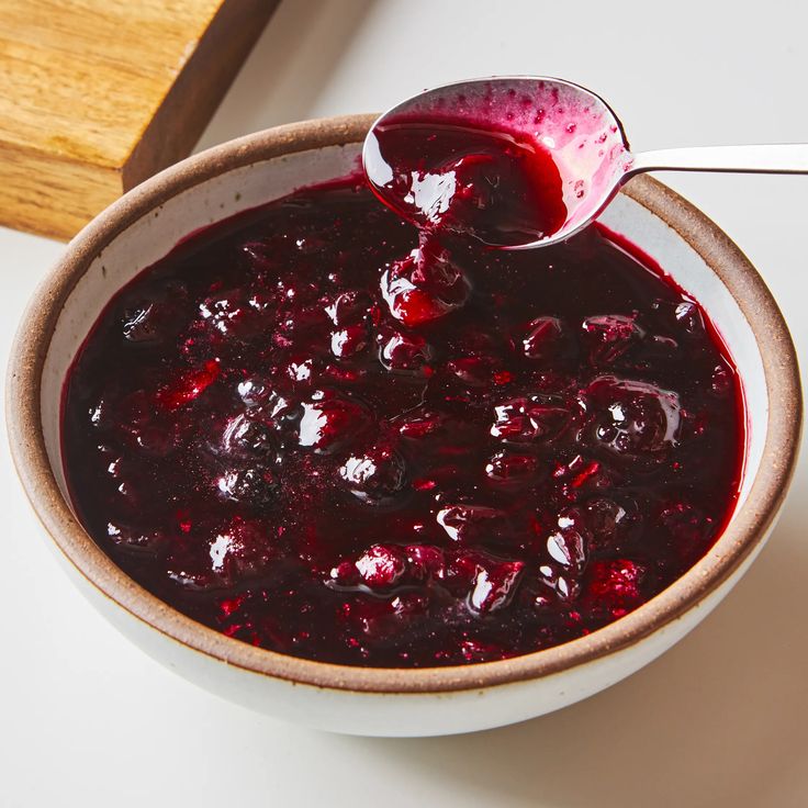 a bowl filled with cranberry sauce next to a wooden spoon