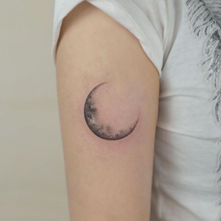 a small crescent moon tattoo on the right arm