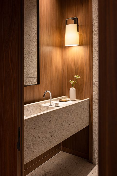 a bathroom sink sitting under a mirror next to a wooden wall with a light on it