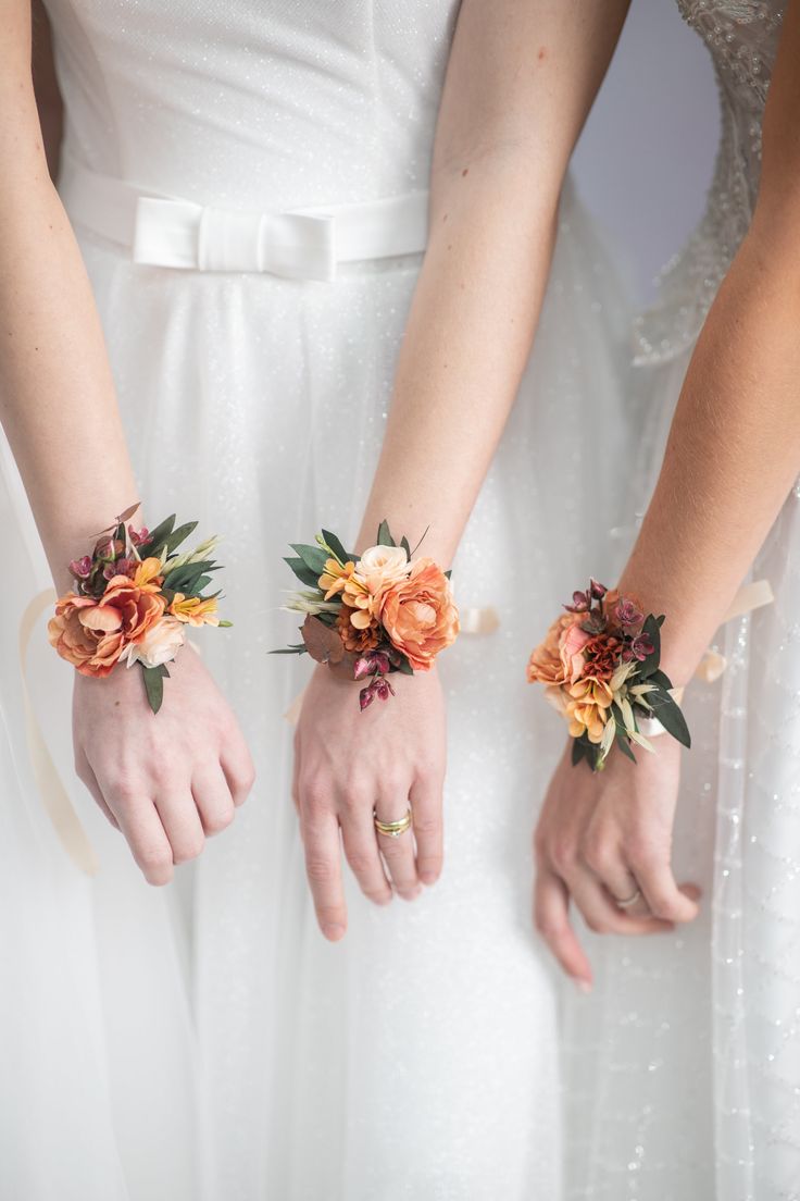 two brides holding hands with flowers on their wristbands in front of them