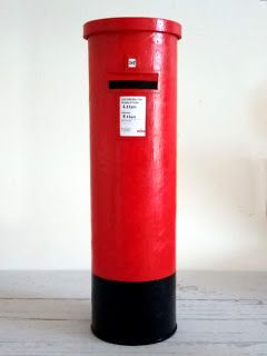 a red and black mailbox sitting on top of a wooden floor next to a white wall