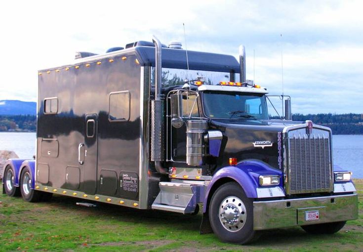 a large semi truck parked on top of a lush green field next to a lake