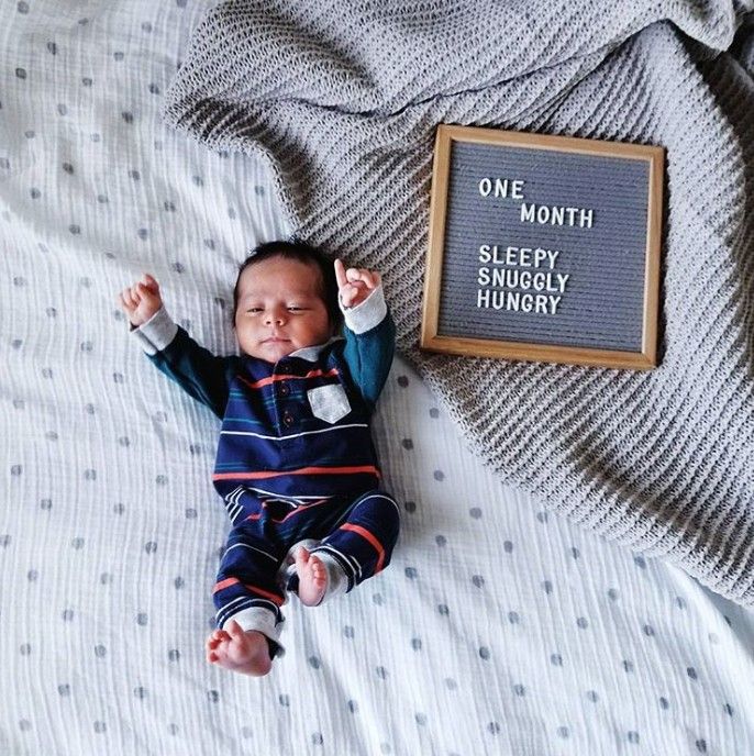 a baby laying on top of a bed next to a sign that says one month sleddy snugglely hungry