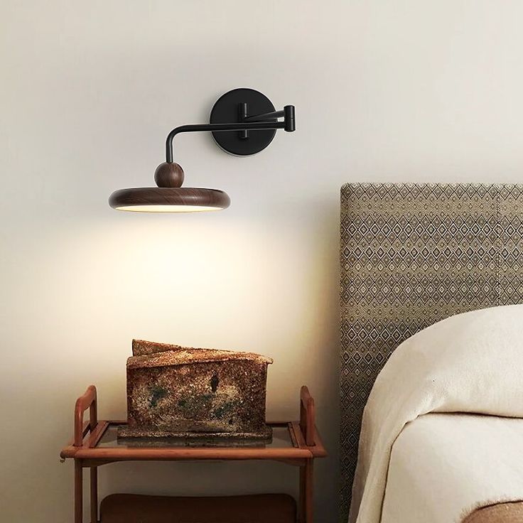 a bedroom with a bed, night stand and lamp on the wall next to it