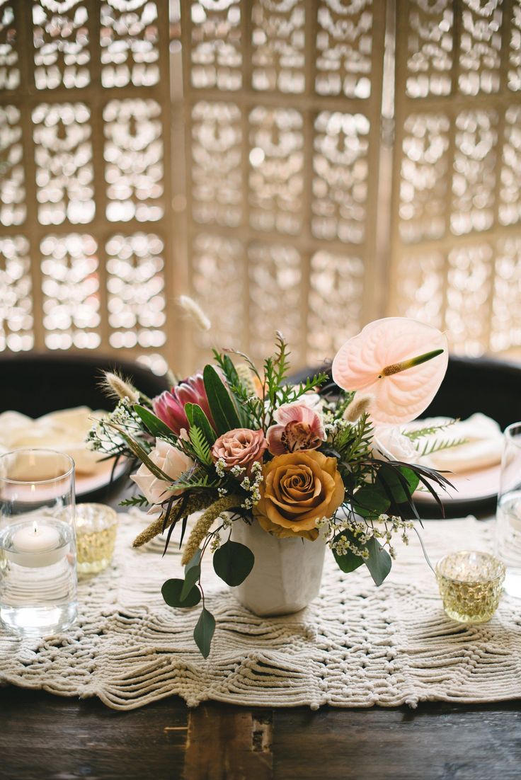 a table topped with a vase filled with flowers and greenery next to plates on top of a wooden table