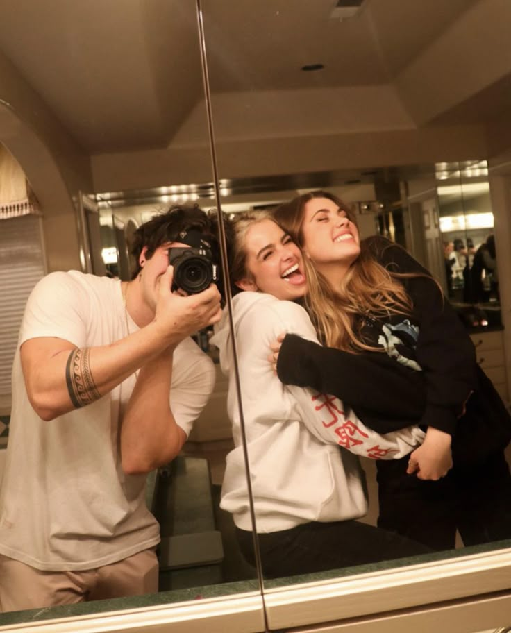 three people taking a selfie in front of a mirror with one person holding a camera