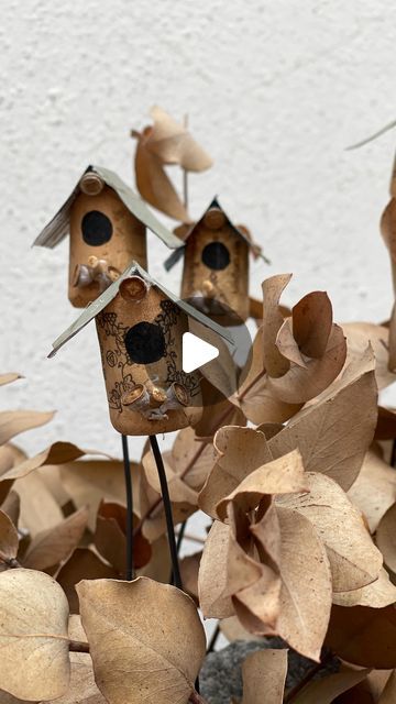 three birdhouses are sitting on top of leaves in front of a white wall and one is made out of wood