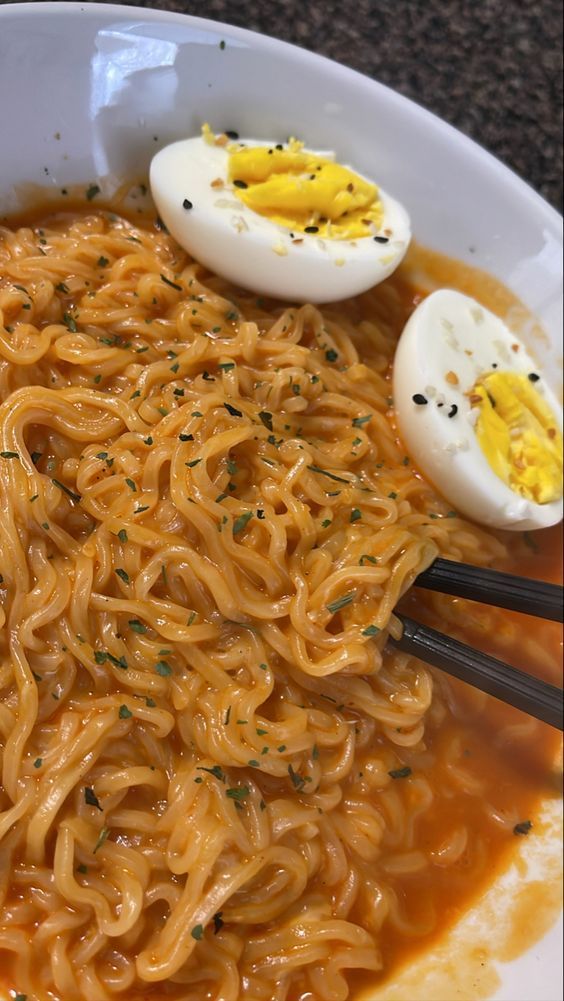 an egg sits on top of noodles in a bowl with chopsticks and two hard boiled eggs