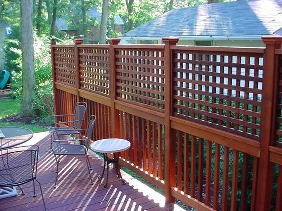 a wooden deck with chairs and table next to the fenced in area that is surrounded by trees