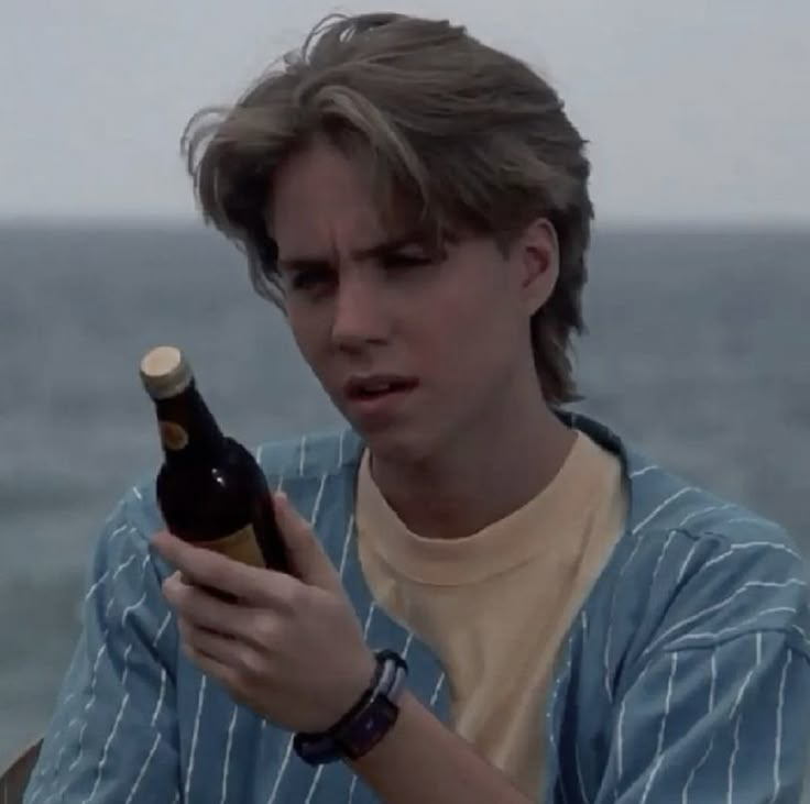 a young man holding a beer bottle and looking at his cell phone