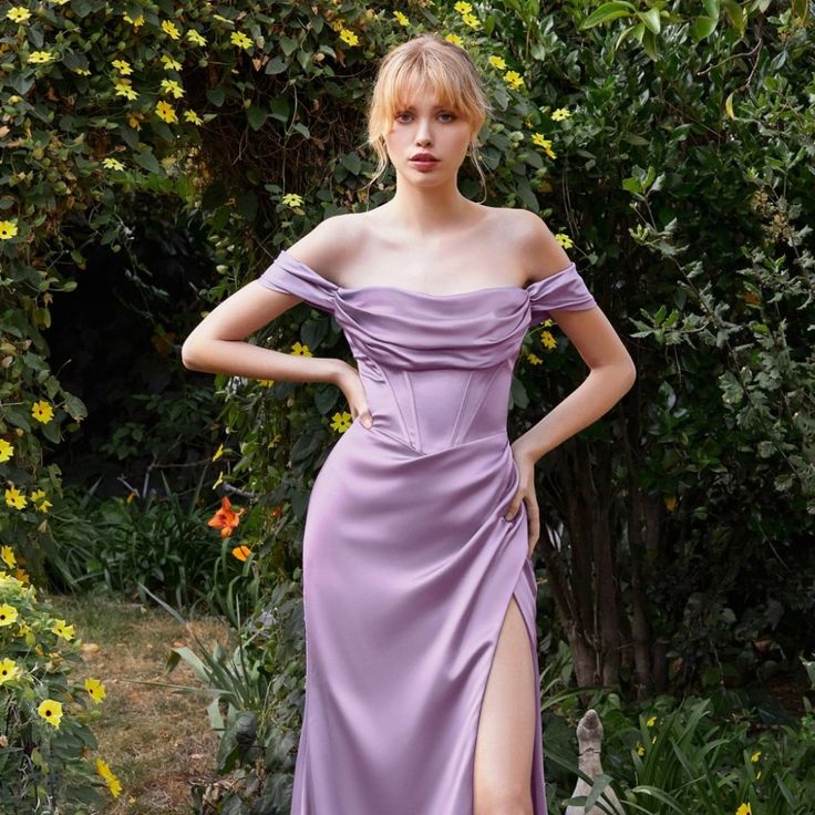 a woman in a purple dress standing next to some bushes and trees with yellow flowers