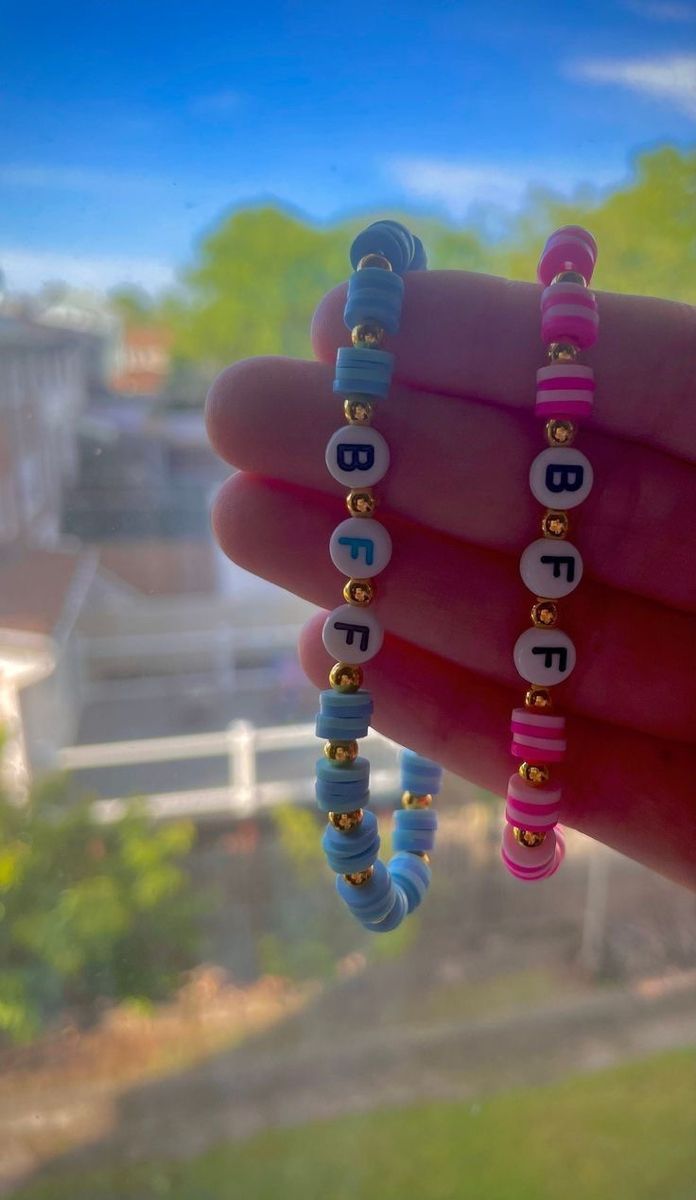 a hand holding two bracelets with letters on them and beads hanging from the end