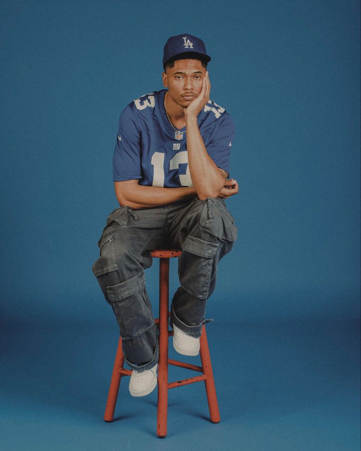 a man sitting on top of a wooden stool wearing a football uniform and holding his hand to his face