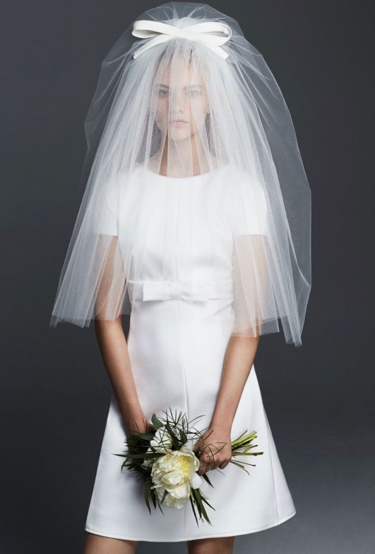 a woman in a white wedding dress holding a bridal veil over her head and flowers