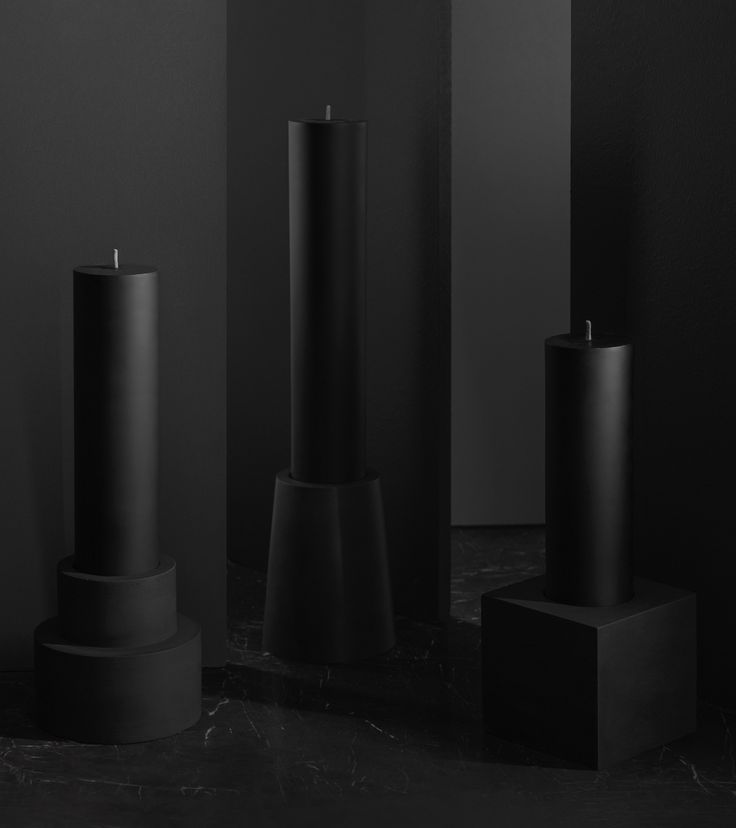 three black candles sitting on top of pedestals in a room with dark walls and flooring