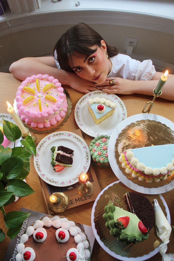 a woman sitting at a table with several cakes and candles in front of her face