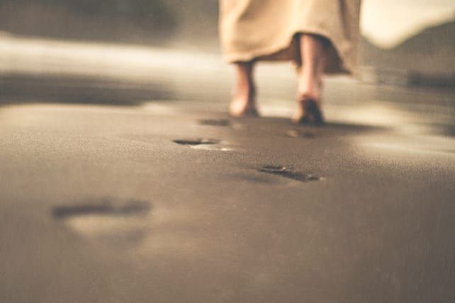 a woman walking on the beach with her feet in the sand