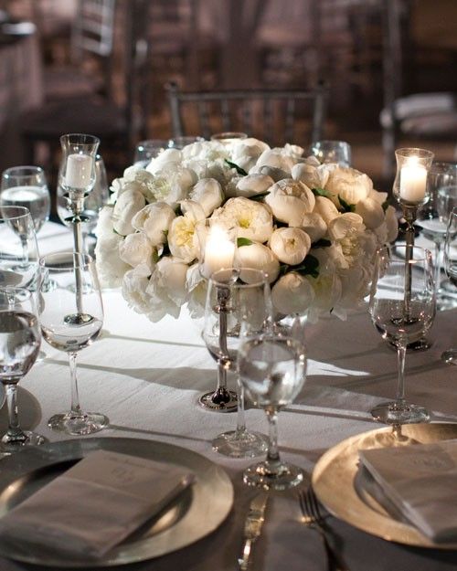 a centerpiece with white flowers and candles is displayed on a table set for an elegant dinner