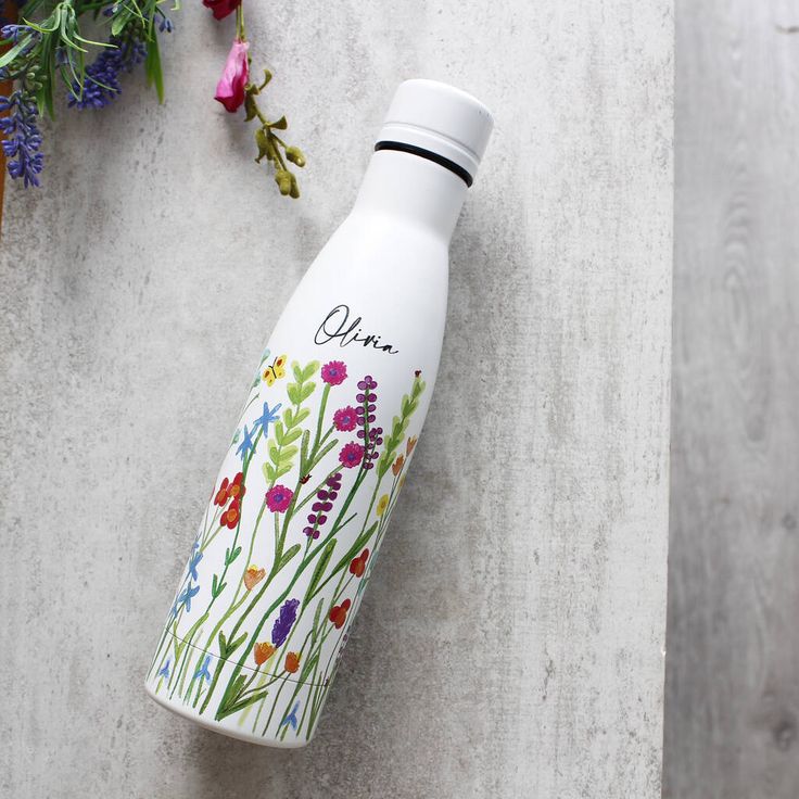 a white water bottle sitting on top of a cement floor next to flowers and plants