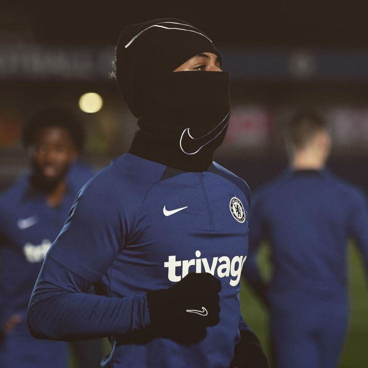 a man wearing a black face mask on top of his head in the middle of a soccer field