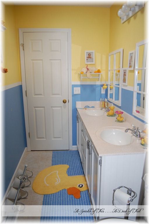 a bathroom with yellow rubber ducky rug on the floor and blue walls, along with two sinks