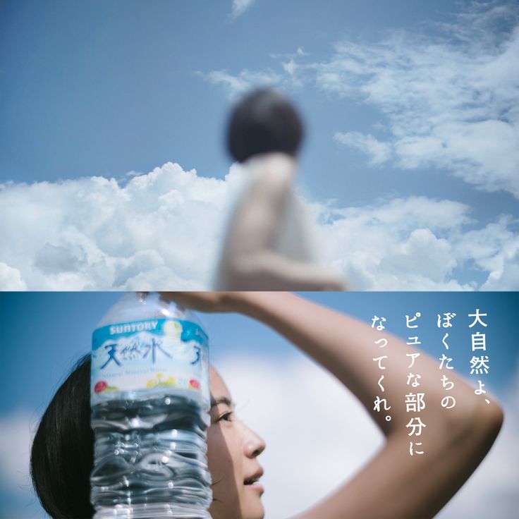 a woman holding a bottle of water in front of her face with the sky and clouds behind her