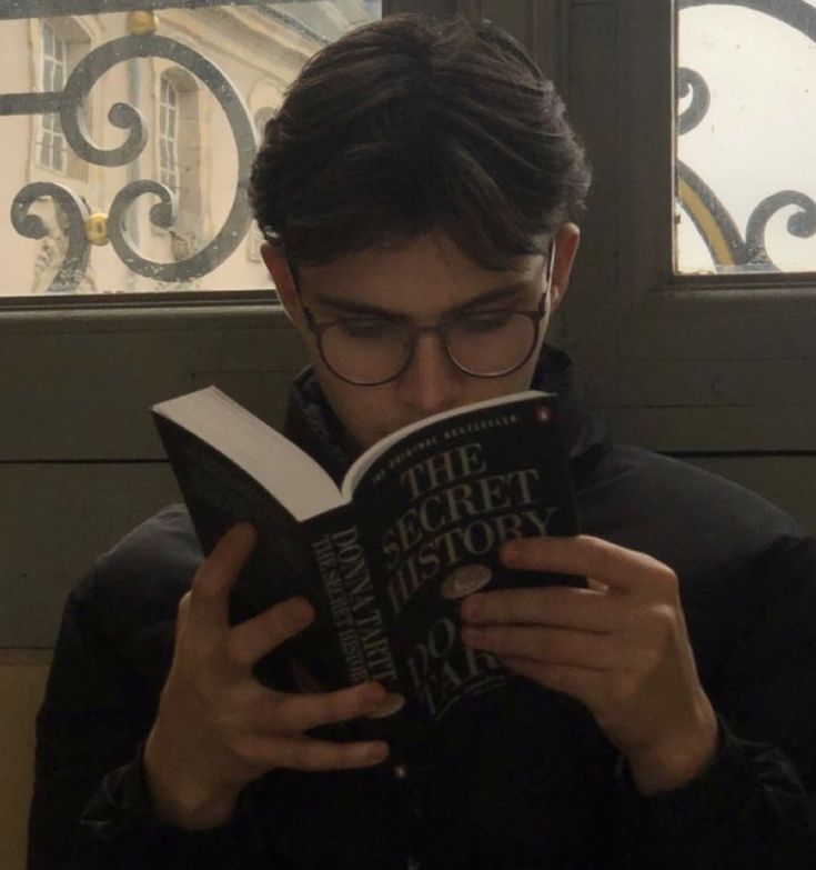 a young man reading a book in front of a window