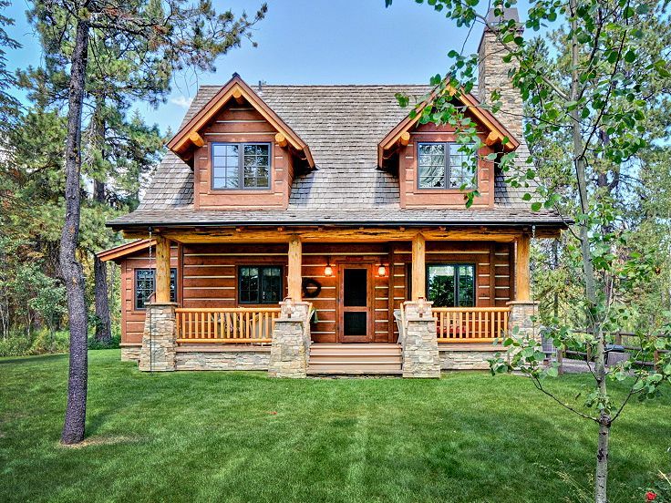 a large log home in the woods with porches and stonework on the front