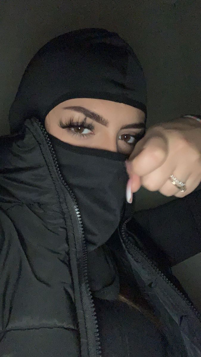 a woman wearing a black hoodie pointing at the camera with her finger on her nose