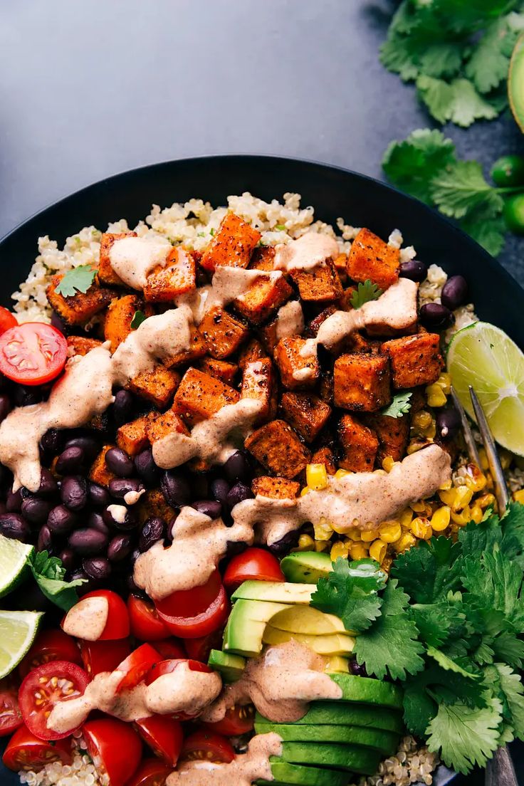 a black plate topped with chicken, rice and veggies next to lime wedges