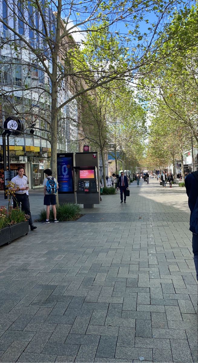 people are walking down the sidewalk in an urban area with tall buildings on either side