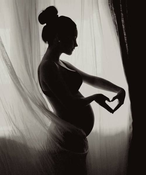 a black and white photo of a pregnant woman with her hands in the shape of a heart