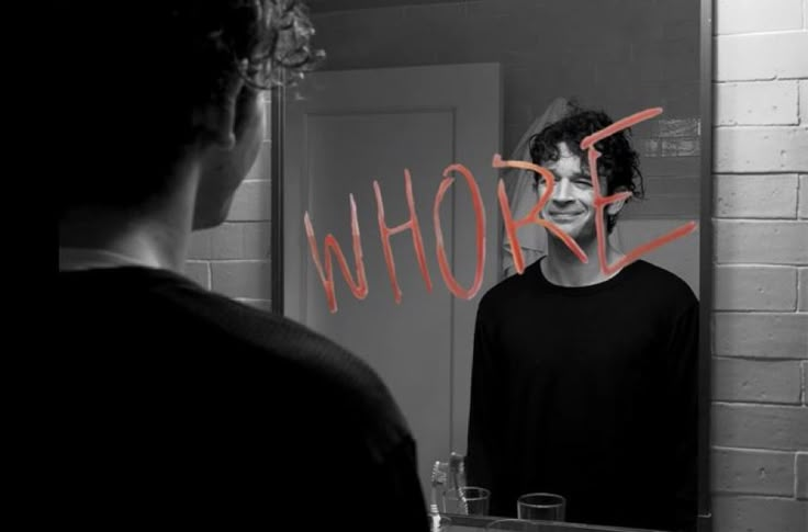 a man standing in front of a mirror with the words who? painted on it