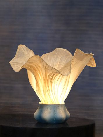 a white flower sitting on top of a table next to a black round base with a light in it