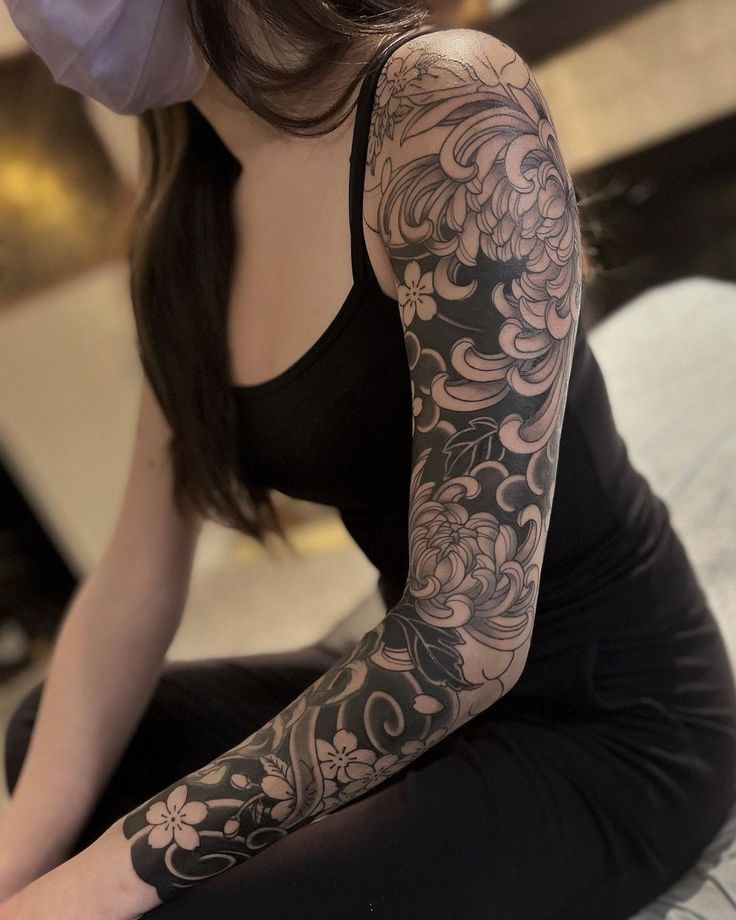 a woman sitting on top of a bed with tattoos on her arm and arms,