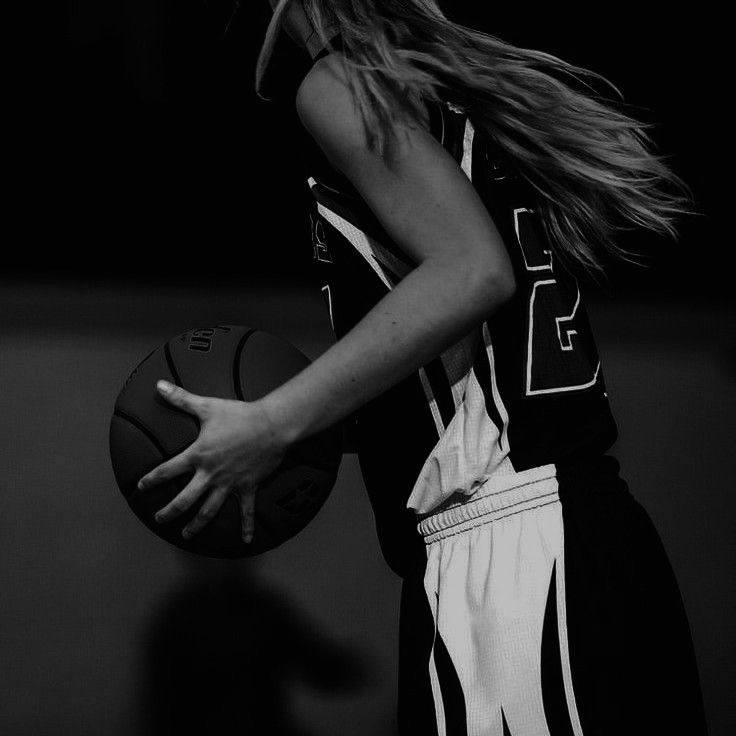 a woman holding a basketball in her right hand and wearing a black and white uniform