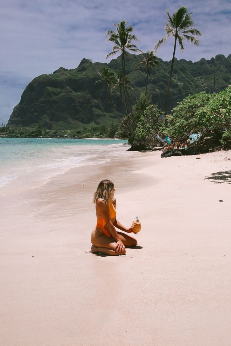 a woman sitting on top of a sandy beach next to the ocean with palm trees