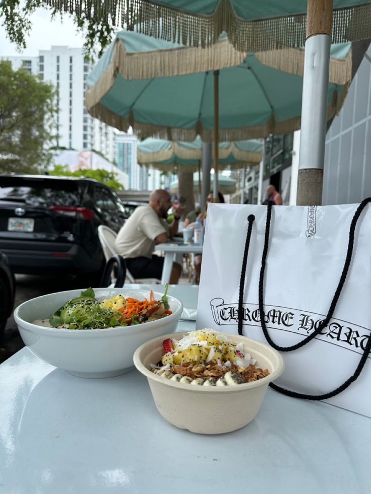 a bowl of salad and a bag on a table in front of an umbrella outside