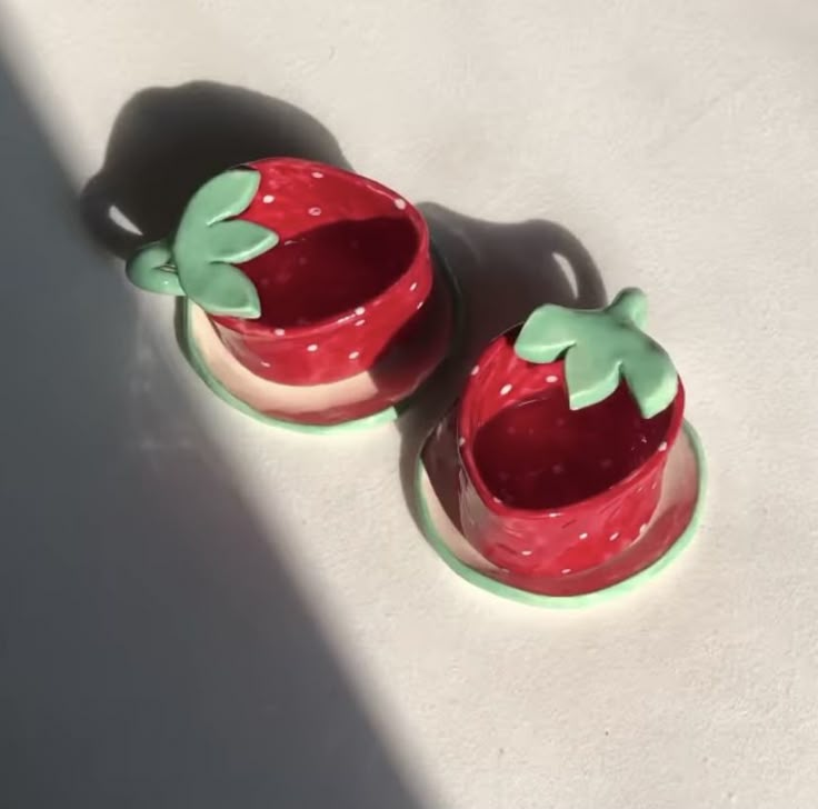 two strawberry shaped ceramic containers sitting on top of a table