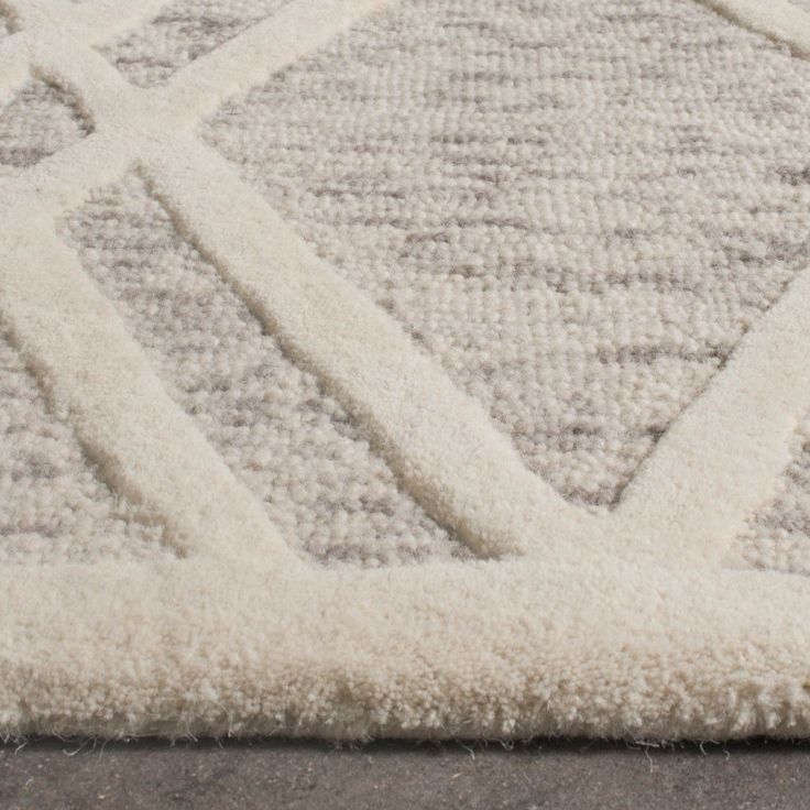 a white rug with diamond shapes on the top and bottom, in front of a gray floor