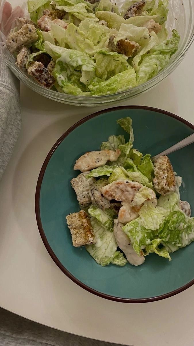 a salad with lettuce and chicken in a bowl next to a woman's hand